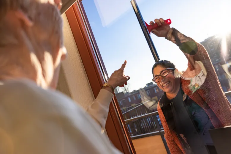 Thuiszorg medewerker zeemt vrolijk de ramen